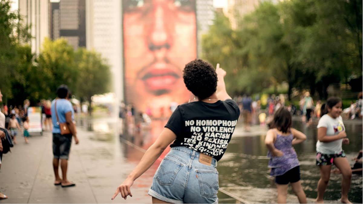 Personas jugando y disfrutando de los juegos de agua en Crown Fountain en Millennium Park de Chicago, rodeadas de árboles y edificios de gran altura.
