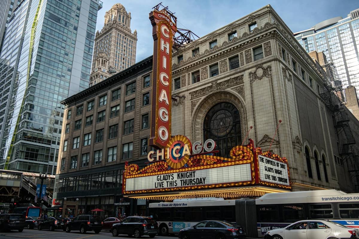 Vista a nivel de calle del icónico Chicago Theatre con su marquesina brillantemente iluminada, rodeado de edificios de la ciudad y tráfico durante el día.