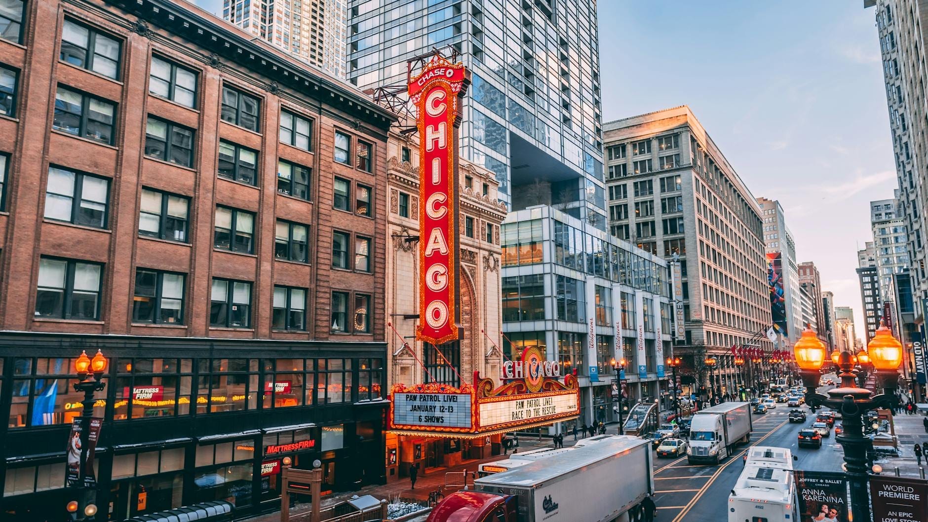 Vista diurna dell'iconica insegna al neon verticale del Chicago Theatre su State Street, circondata dal traffico cittadino e dai grattacieli del centro di Chicago.