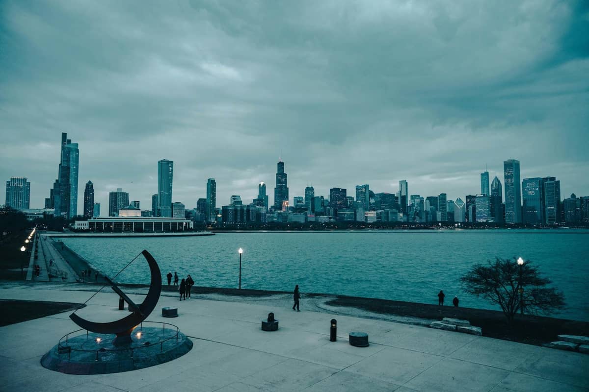 Vista del horizonte de Chicago desde un sendero junto al lago con esculturas y personas, con vistas al lago Michigan en un día nublado.