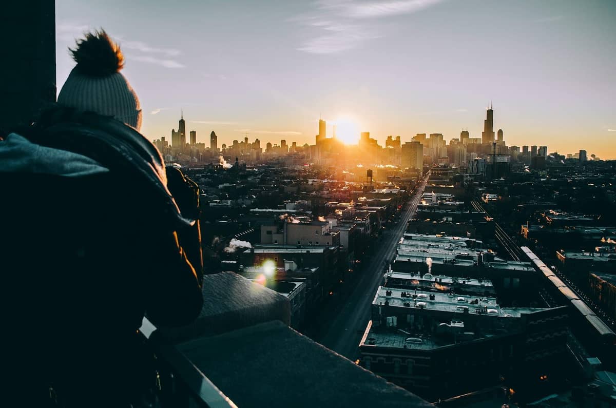 Persona con ropa de invierno de pie en una azotea con vistas al horizonte de Chicago al amanecer con rascacielos y panorámica de la ciudad.