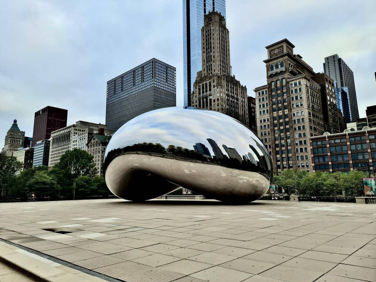 Die Skulptur Cloud Gate, bekannt als 'The Bean', mit den Wolkenkratzern von Chicago dahinter im Millennium Park an einem fast menschenleeren Morgen.