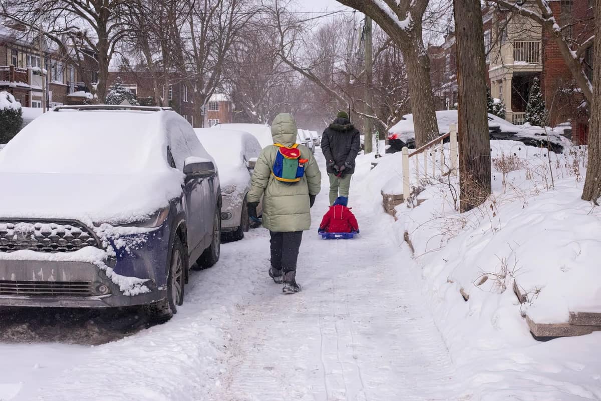 Bambini e adulti che camminano e trascinano una slitta lungo una strada residenziale di Chicago coperta di neve dopo una tempesta invernale.
