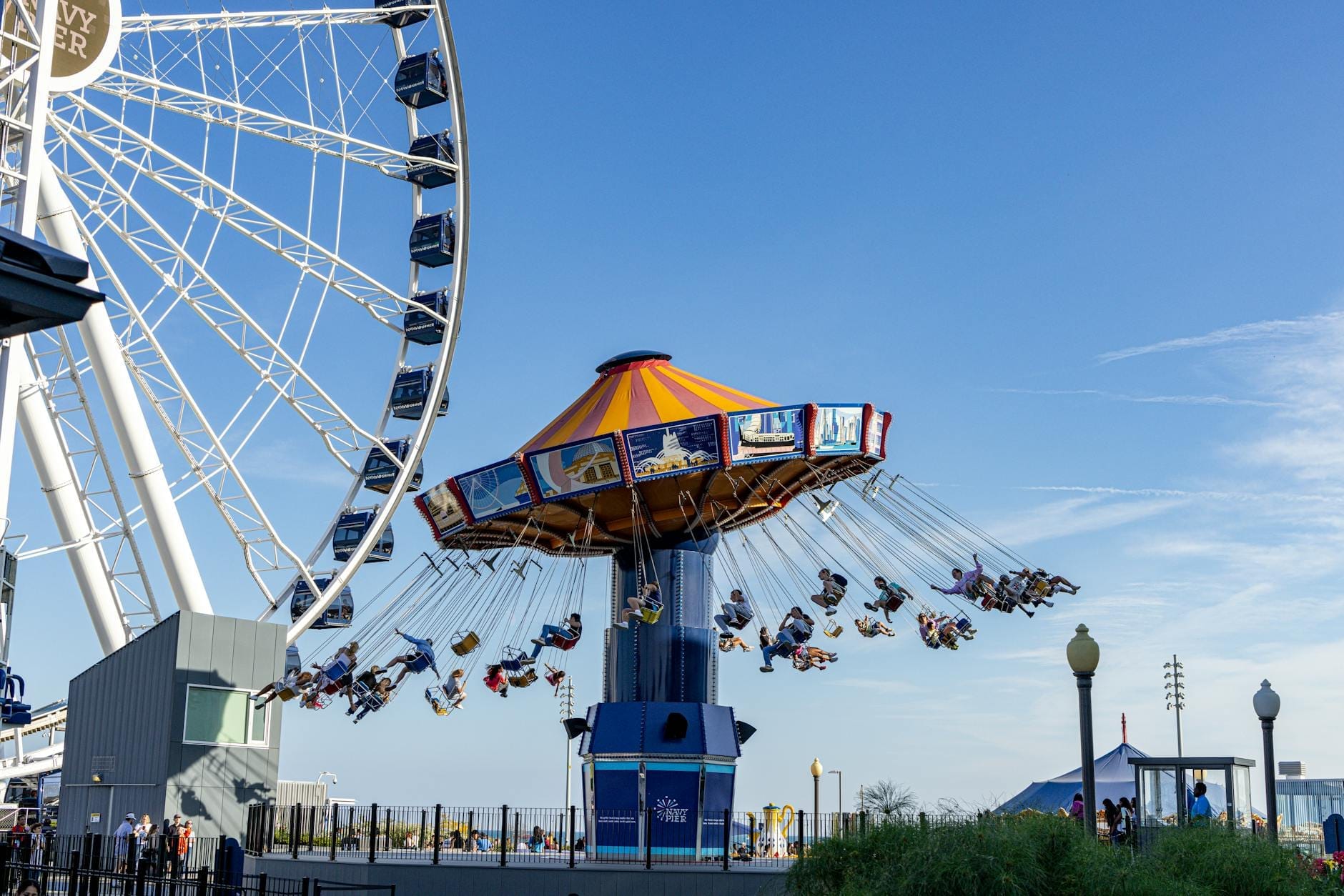 Crianças e famílias em um carrossel de balanços colorido próximo a uma grande roda-gigante no Navy Pier de Chicago em um dia ensolarado.