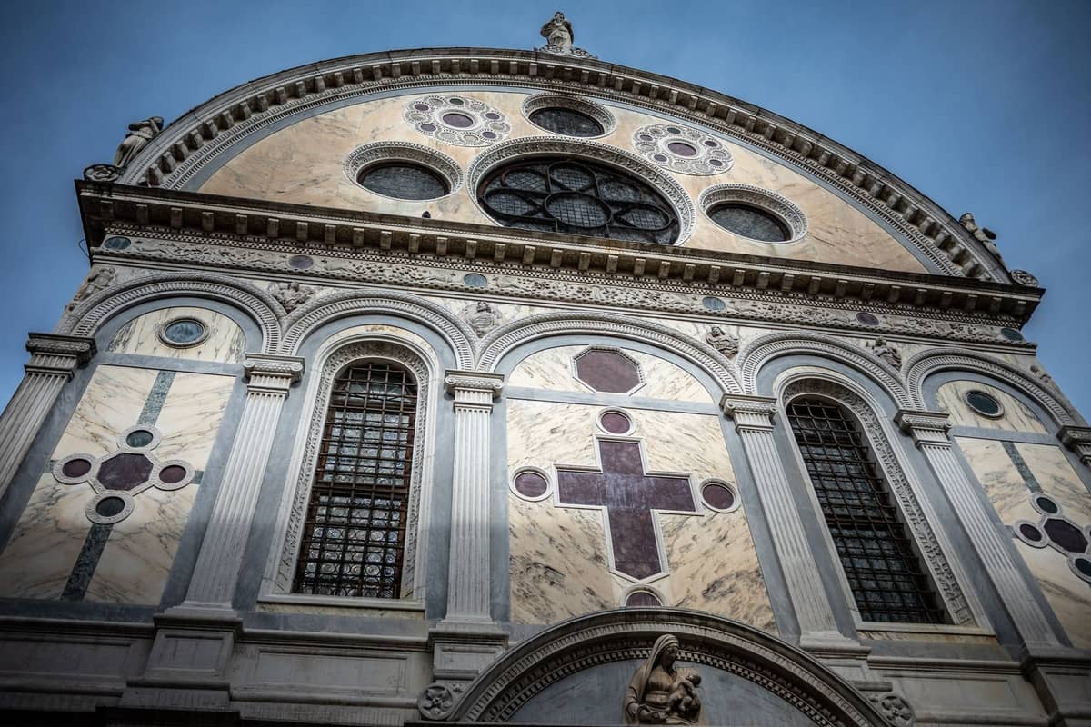 Nahaufnahme der Marmorfassade der Chiesa di Santa Maria dei Miracoli in Venedig mit Renaissance-Architektur und polychromem Steinwerk vor blauem Himmel.