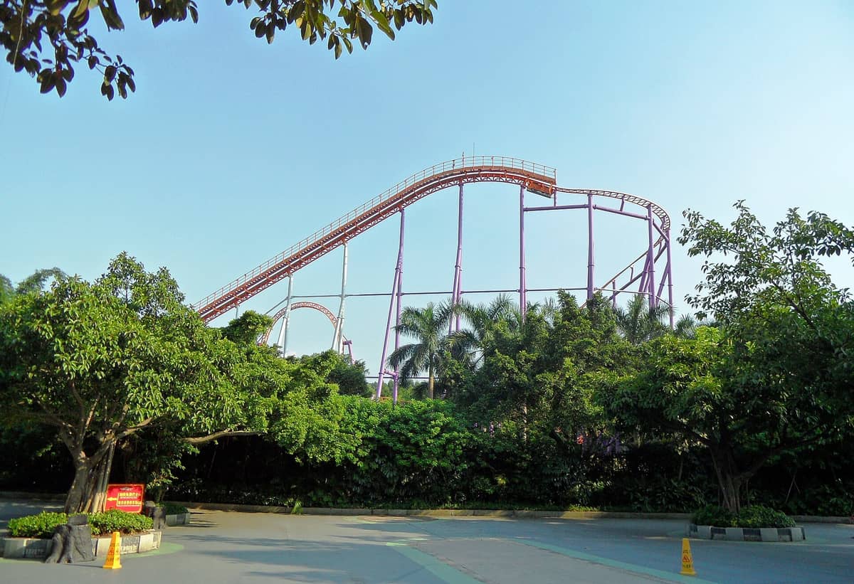 Roller coaster rising above lush trees at Chimelong Paradise amusement park in Guangzhou on a clear sunny day.
