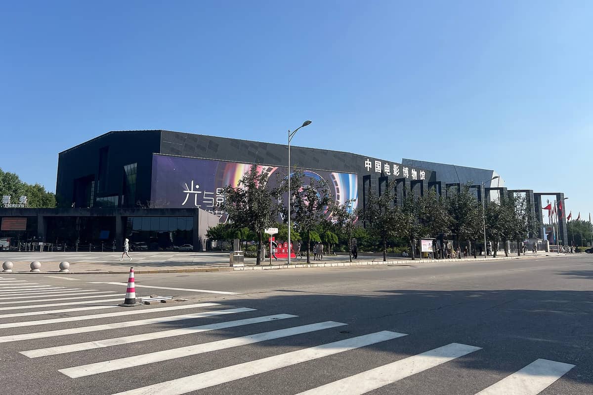 Weitwinkelansicht des modernen, schwarz-kantigen Außenbaus des Chinesischen Nationalen Filmmuseums mit großen Fenstern und Eingang, von einer Straße in Peking aus gesehen.