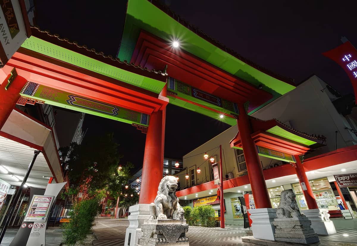 Nocny widok na główną chińską bramę i kamienne lwy strażnicze w Chinatown Brisbane na Duncan Street, z lampionami zwisającymi wzdłuż deptaka.
