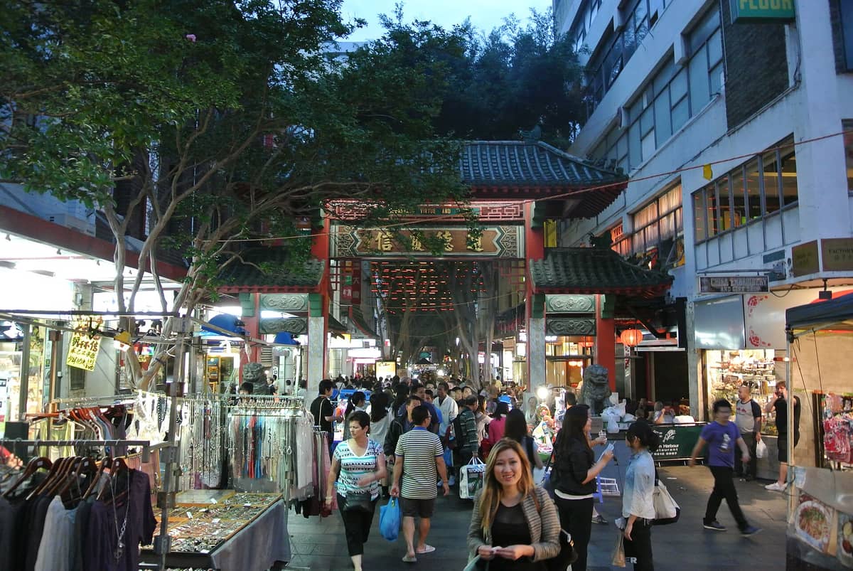 Dixon Street a Sydney animata in una serata affollata: il caratteristico portale ornamentale, la folla che passeggia e le bancarelle del mercato lungo la via pedonale.