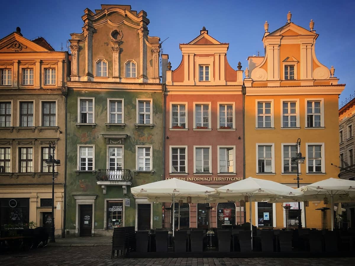 Kolorowe zabytkowe kamienice z ozdobnymi fasadami na Rynku Starego Miasta w Warszawie, popołudniowe słońce, ogródek kawiarniany z parasolami na pierwszym planie.