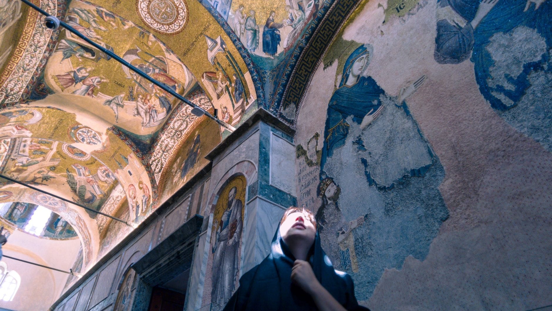 Un visitatore che guarda verso l'alto ammirando i mosaici e gli affreschi bizantini dorati che decorano le pareti e i soffitti interni della Chiesa di Chora a Istanbul.