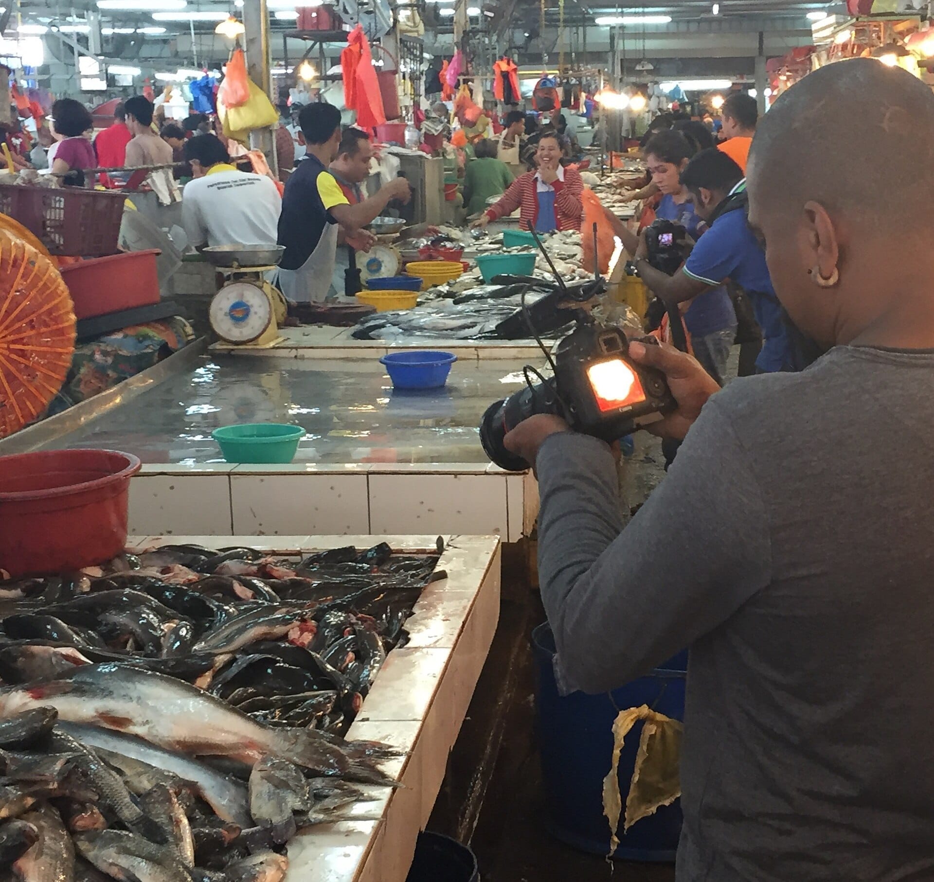 Fresh fish on display at Chow Kit Market with vendors and shoppers under bright market lights in a bustling indoor setting.