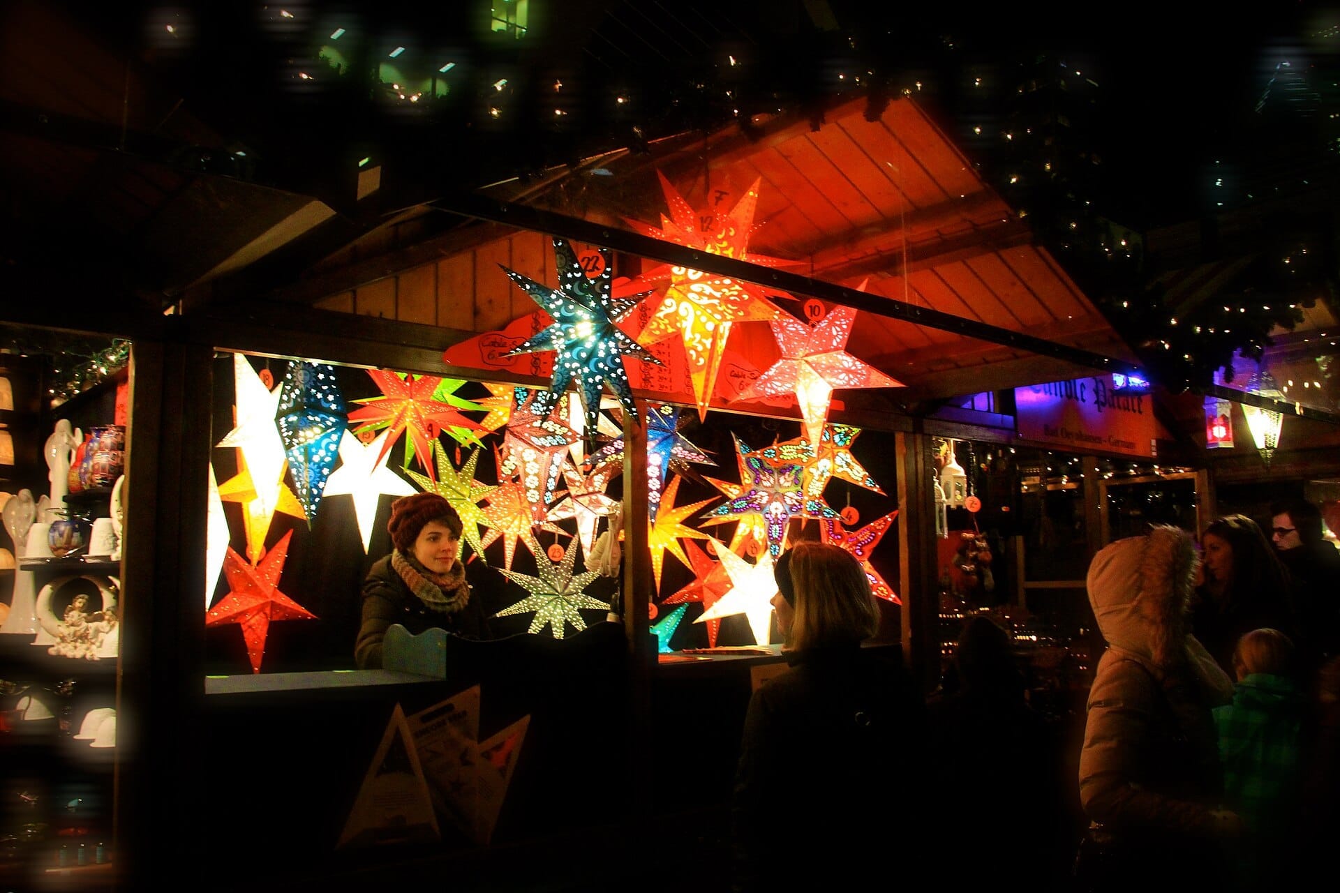 Una bancarella del Christkindlmarket Chicago brillantemente illuminata di notte, decorata con coloratissime lanterne a stella e frequentata da visitatori imbacuccati in abiti invernali.