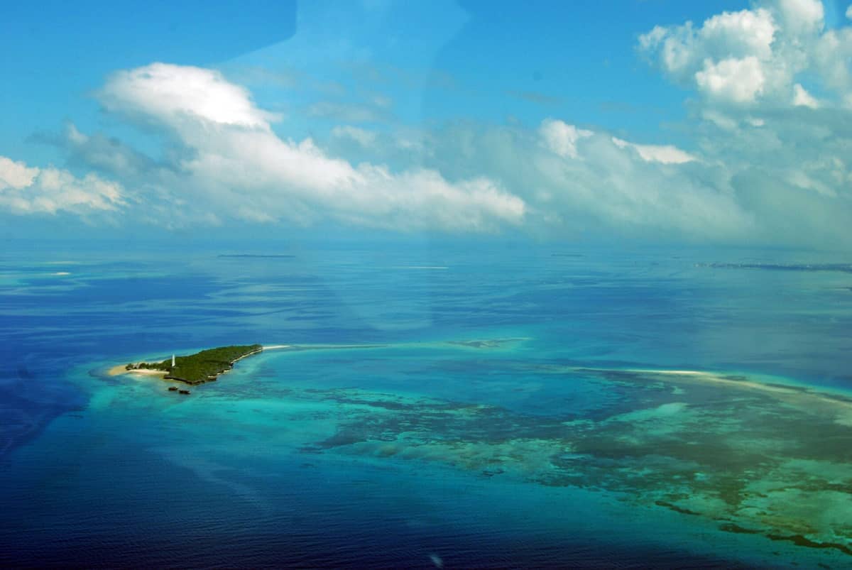 Widok z lotu ptaka na Chumbe Island Coral Park otoczony turkusowymi wodami, rafami koralowymi i bujną zielenią pod częściowo zachmurzonym niebem na Zanzibarze.