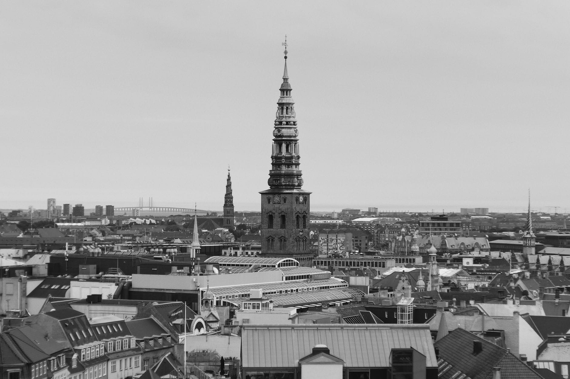 Panoramica in bianco e nero di Copenaghen con la caratteristica guglia a spirale della Chiesa del Nostro Salvatore che si innalza sopra i tetti, dominando il profilo della città.