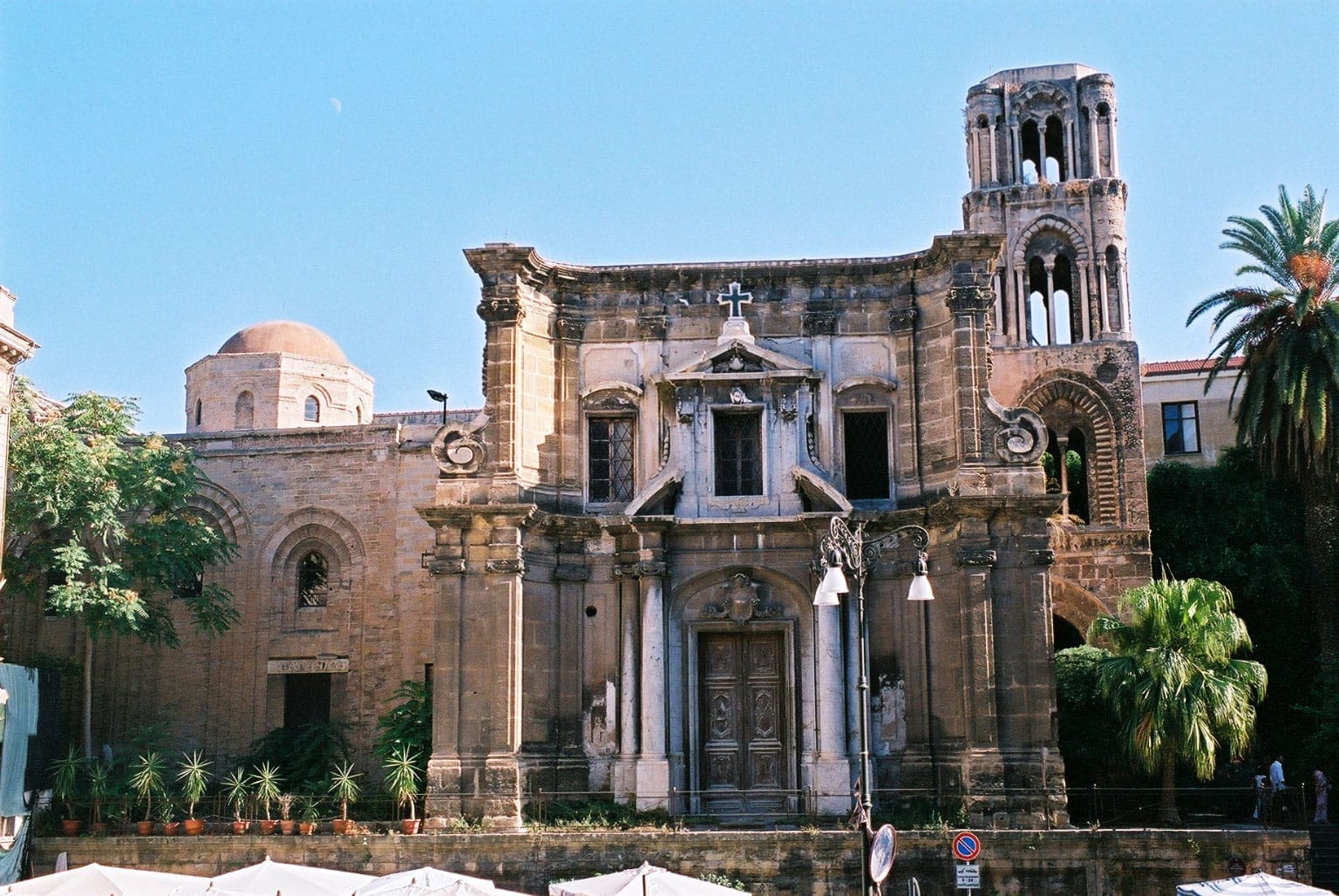 Fassade der Kirche der Martorana in Palermo mit normannischen und byzantinischen Architekturelementen, Bogenfenstern und einem markanten Glockenturm unter klarem Himmel.