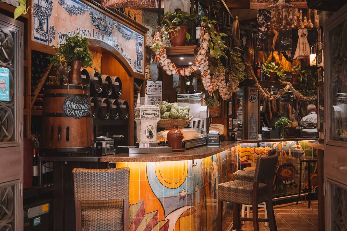 Einladendes Interieur einer gemütlichen italienischen Weinbar mit bunter Dekoration, hängendem Knoblauch, Flaschen und einer Theke mit Hockern.