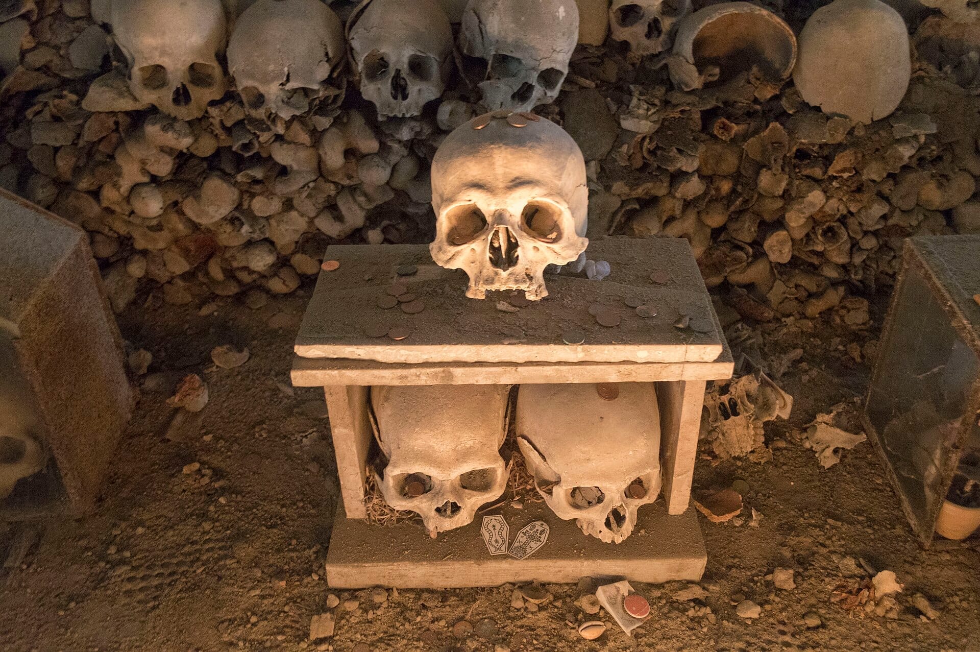 Teschi e ossa umane ammassati in un'esposizione di ossario al Cimitero delle Fontanelle a Napoli, illuminati da una luce dorata e soffusa.