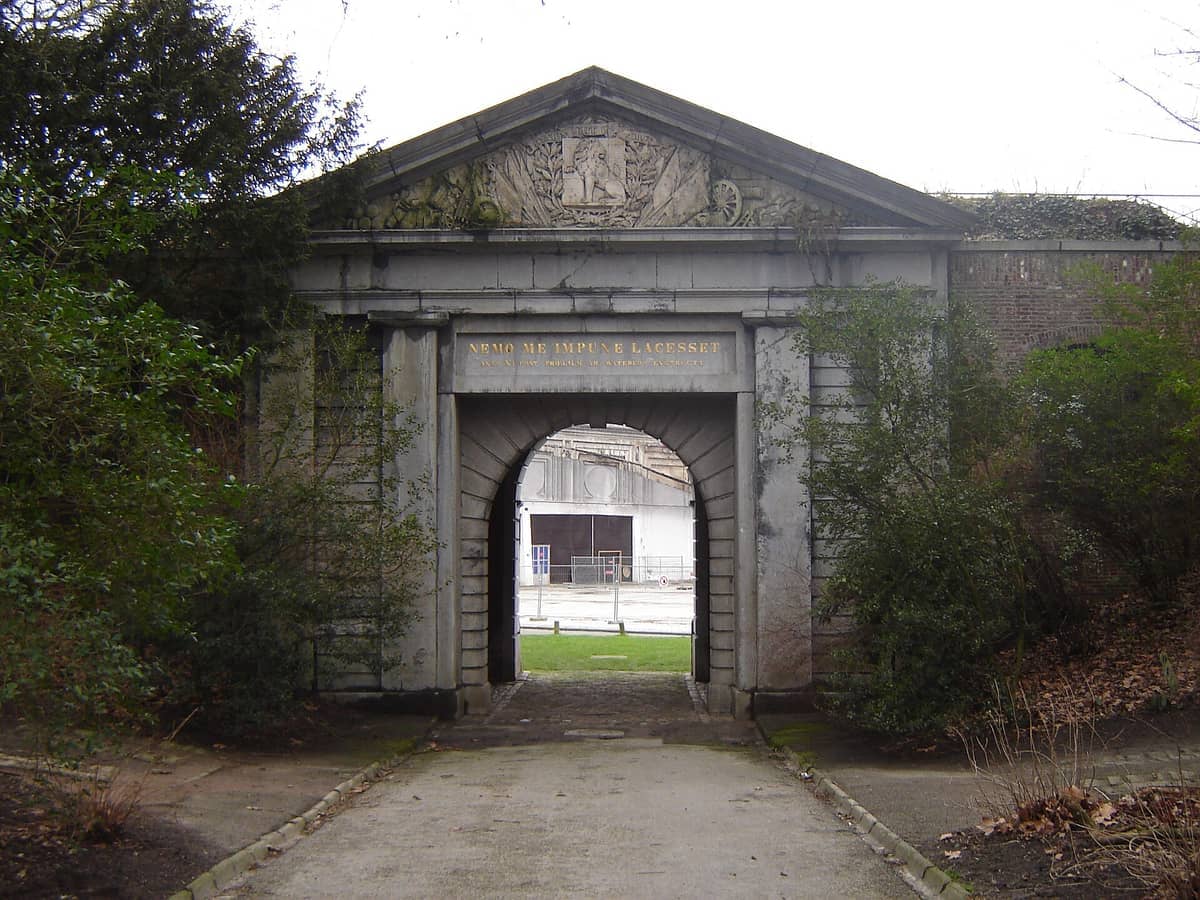 Stone entrance archway at Citadelpark in Ghent, surrounded by green shrubs and trees on a cloudy day.
