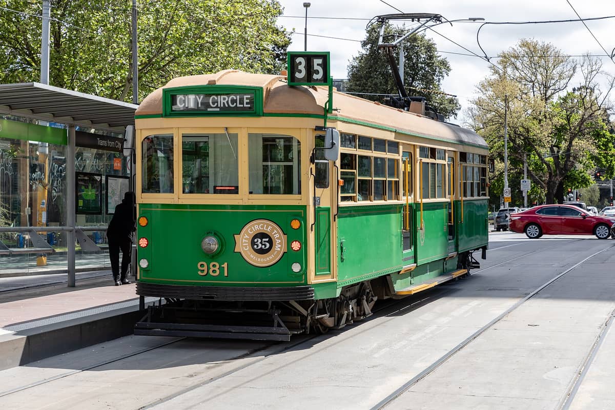 Un tranvía verde y amarillo del City Circle de Melbourne (Ruta 35) en una parada del centro, con árboles y vida urbana de fondo.