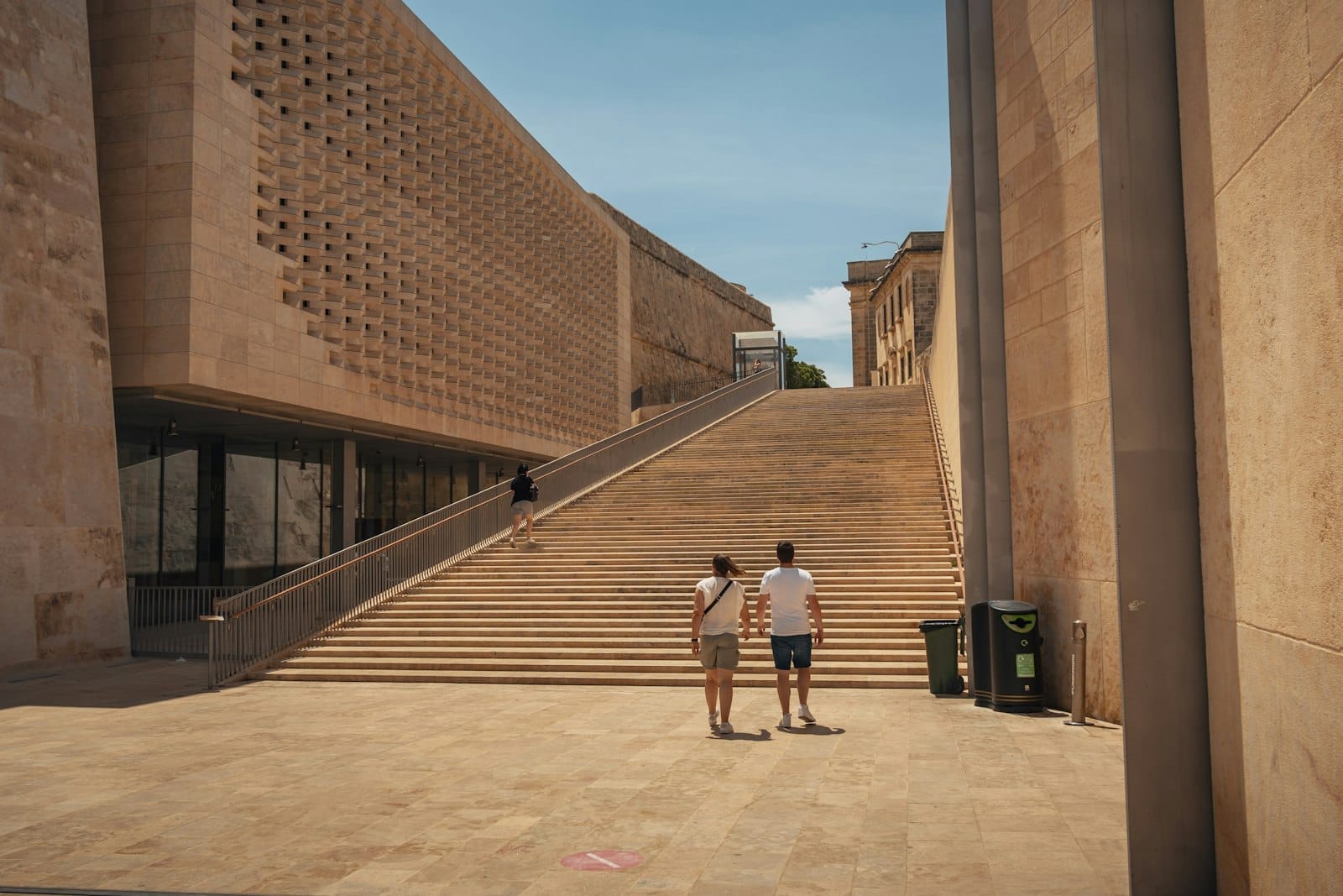 Ampi gradini in pietra incorniciati dal Parlamento e dalla Porta della Città di Valletta di Renzo Piano, con moderne facciate in pietra calcarea sotto un cielo sereno.