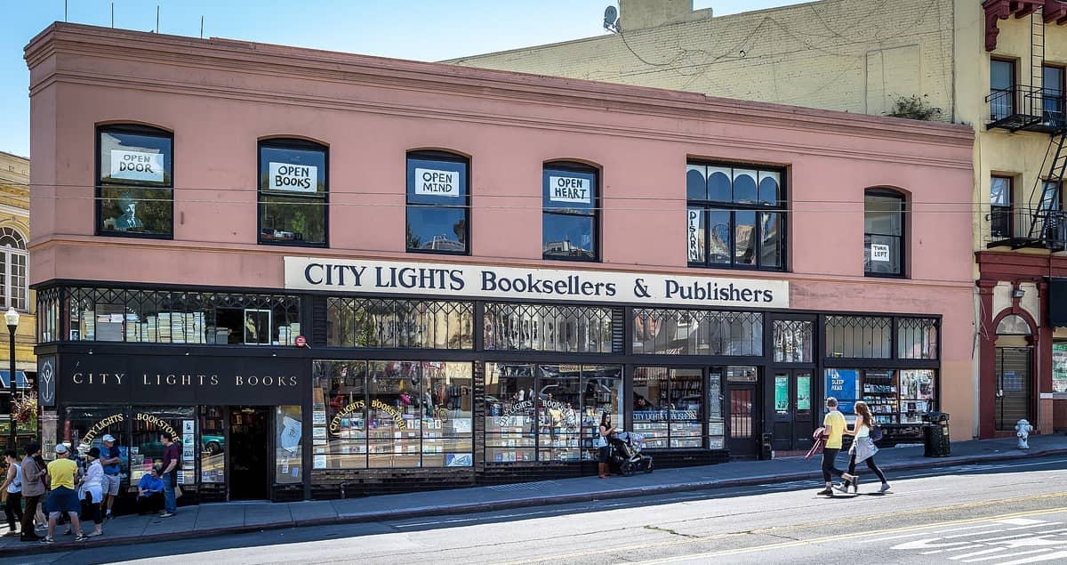 Vista stradale dell'iconico edificio a tre piani di City Lights Booksellers & Publishers con grandi finestre, esposizioni di libri e persone che passeggiano a San Francisco.