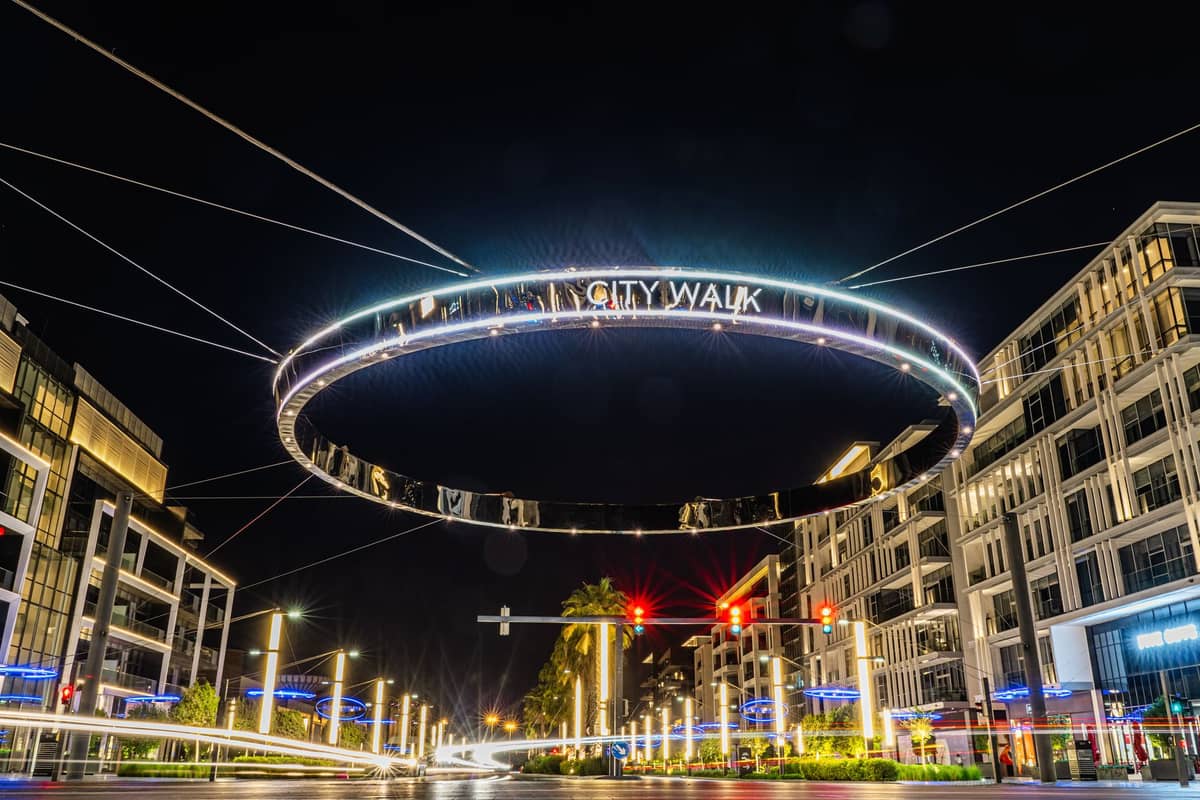 City Walk Dubai at night with a large illuminated circular 'CITY WALK' sign, surrounded by modern buildings and vibrant street lights.