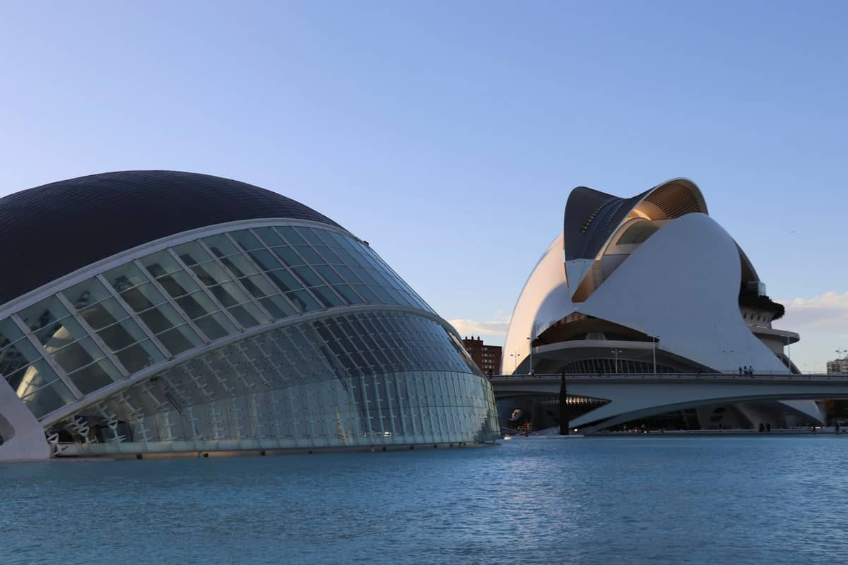 I due iconici edifici bianchi della Ciudad de las Artes y las Ciencias a Valencia, in Spagna, specchiati in una vasca d'acqua sotto un cielo limpido.