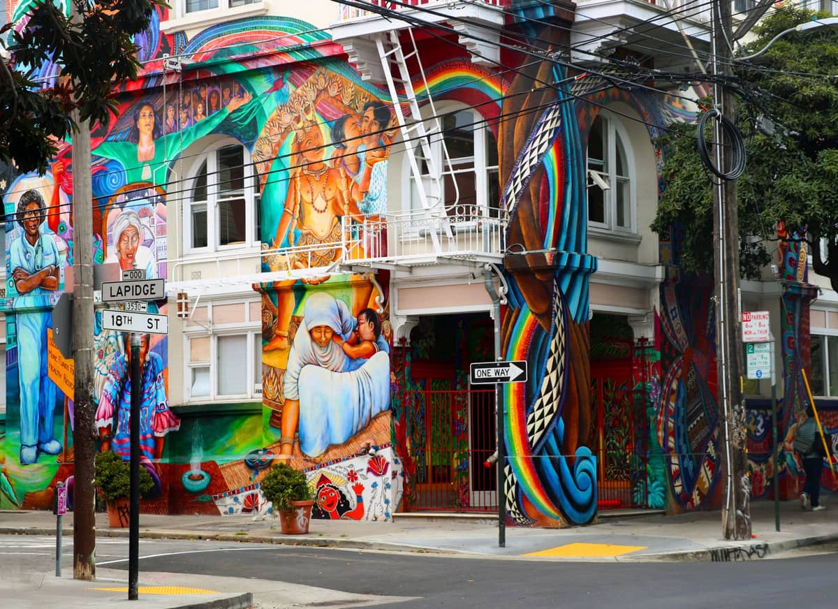 Una vibrante esquina callejera cubierta de grandes murales coloridos con temáticas políticas y culturales, ubicada en el Mission District de San Francisco.