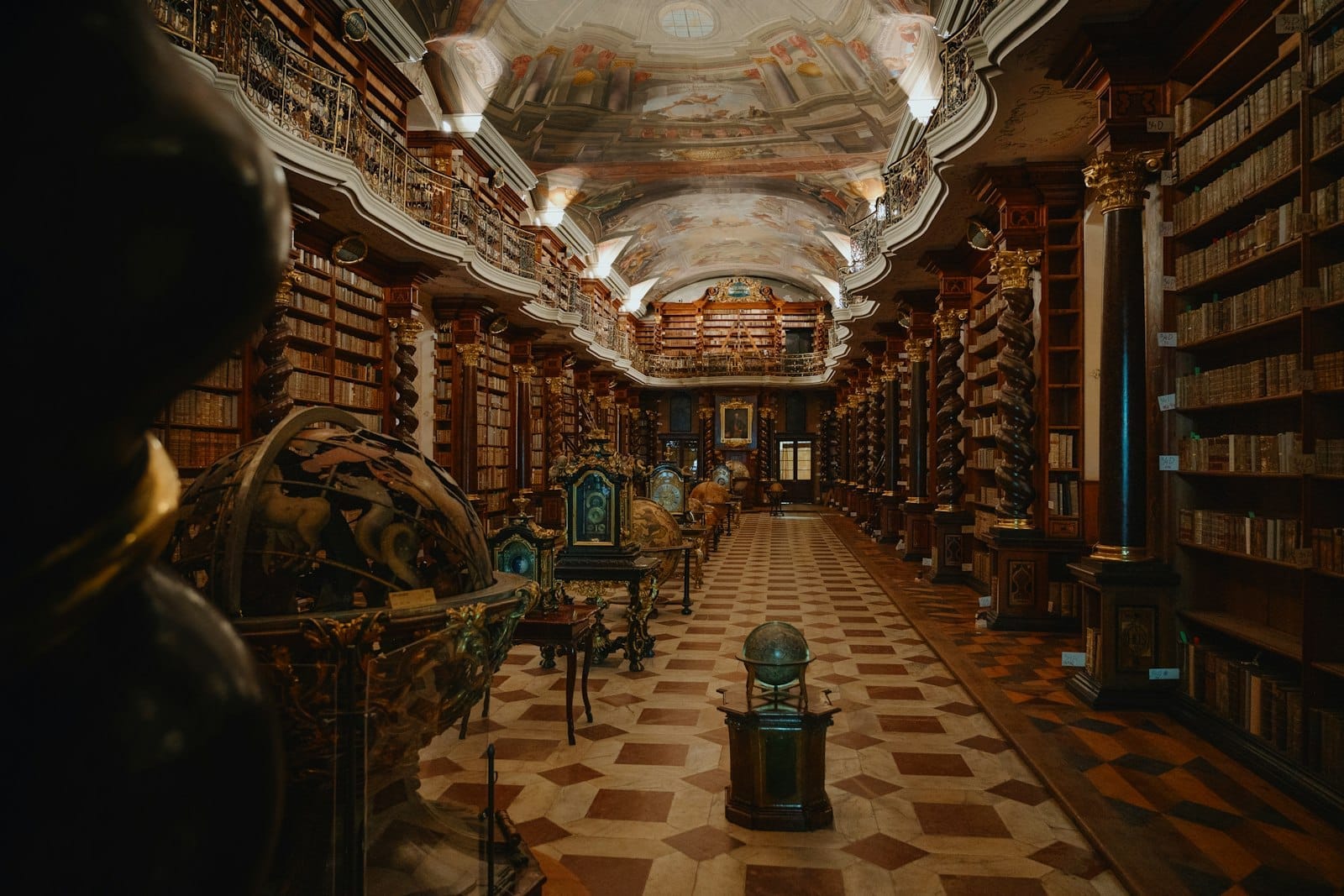 Innenansicht der Barocken Bibliothek des Clementinum in Prag, mit aufwendigen Deckenfresken, Spiralsäulen, antiken Globen und Reihen alter Bücher.