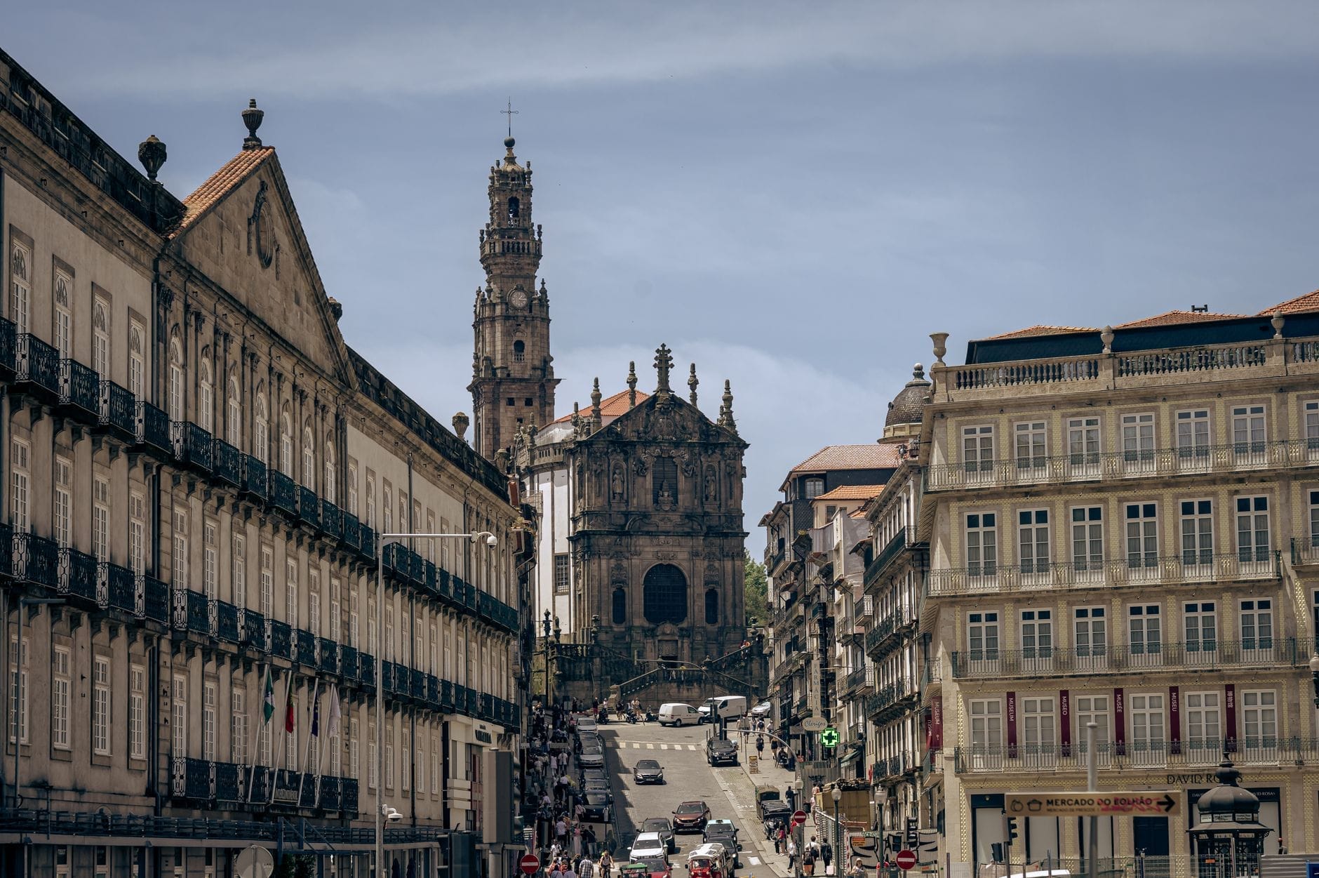 Veduta dalla strada della Chiesa dos Clérigos e del suo alto campanile barocco che si innalza sugli edifici storici di Porto, con cielo terso e passanti.
