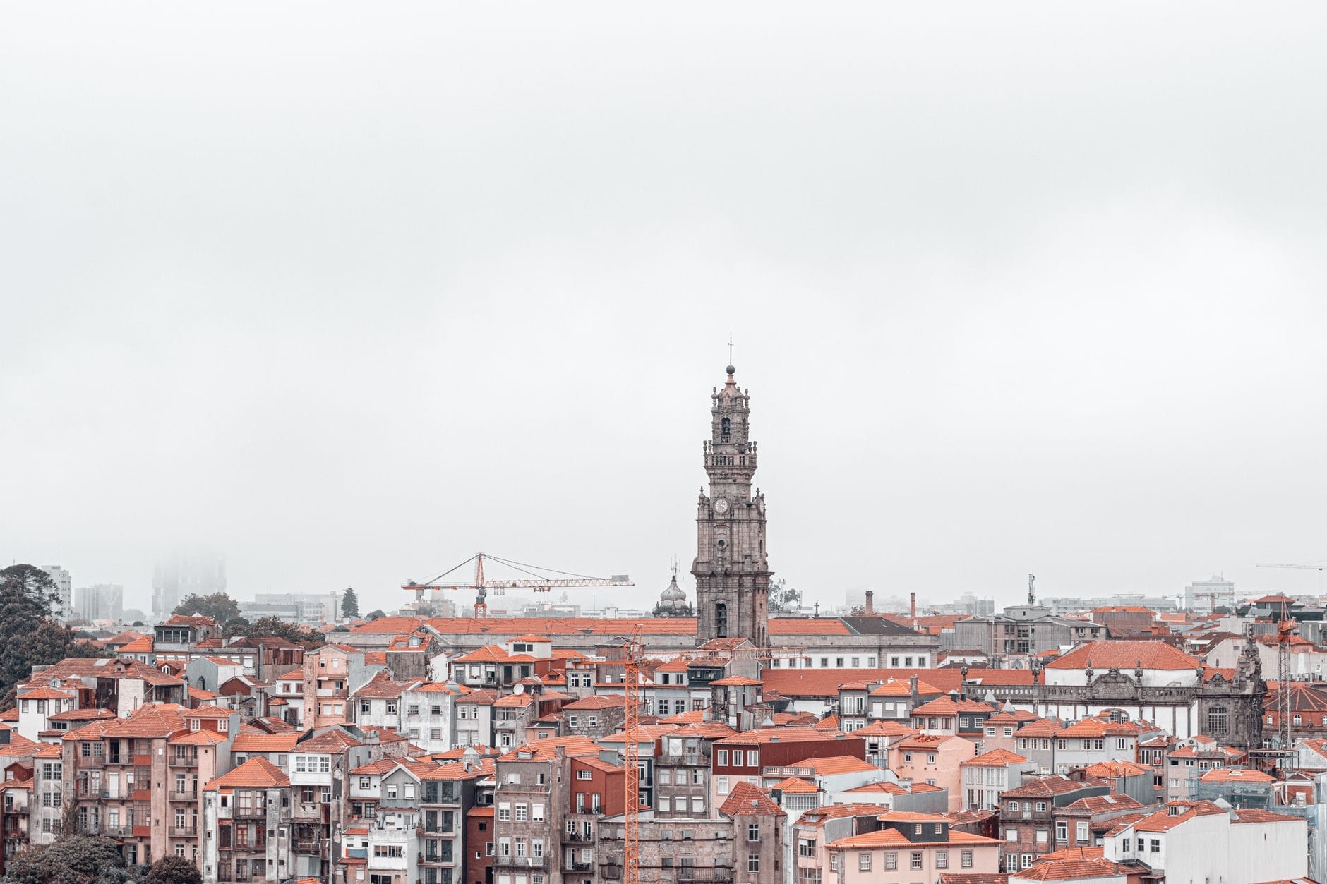 La Torre dos Clérigos si erge sul paesaggio storico di Porto con i tetti color mattone sotto un cielo nuvoloso, dominando lo skyline della città.
