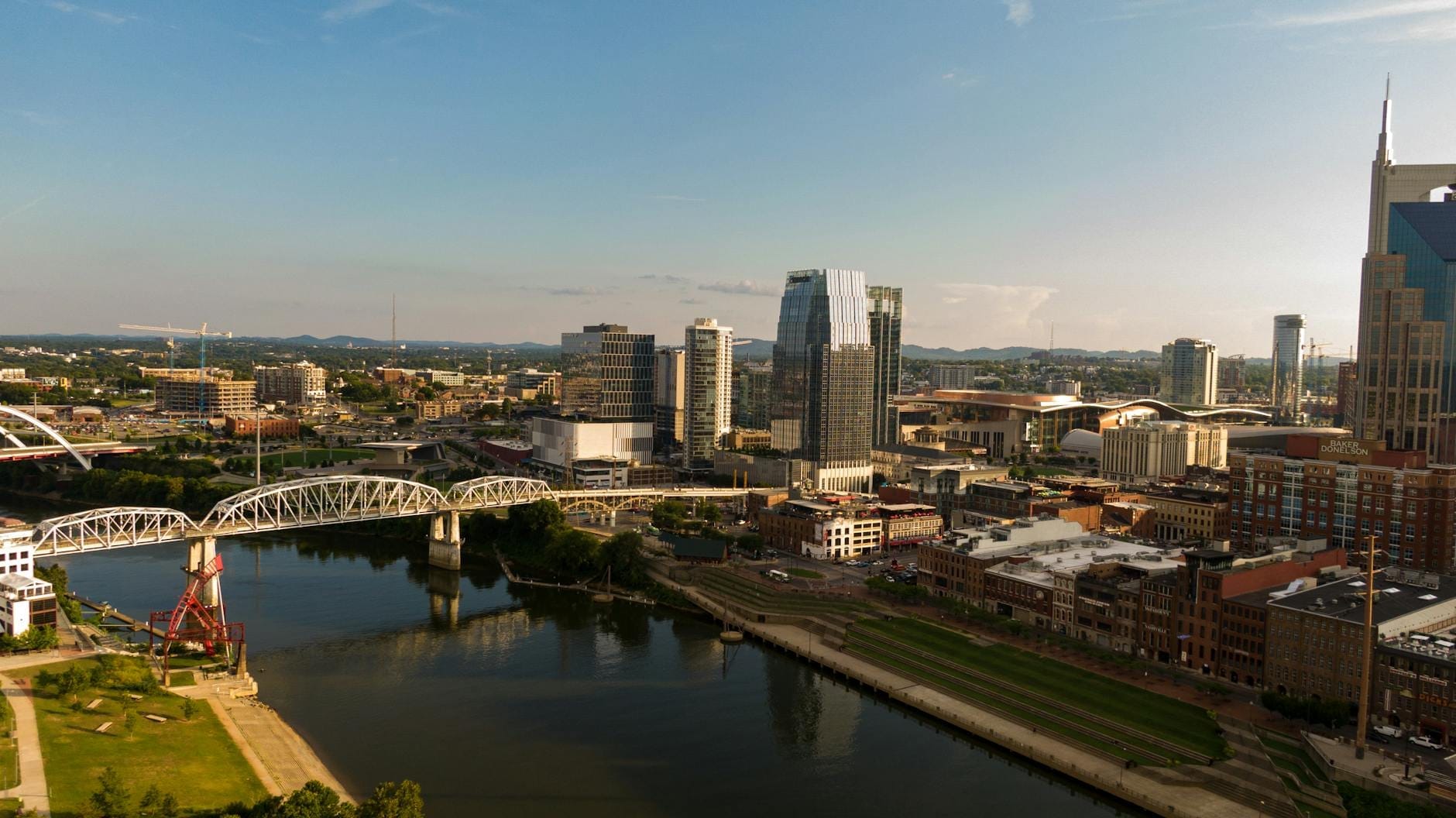 Vista aérea del centro de Nashville con el frente fluvial, puentes y horizonte urbano en un día soleado, ideal para festivales al aire libre.