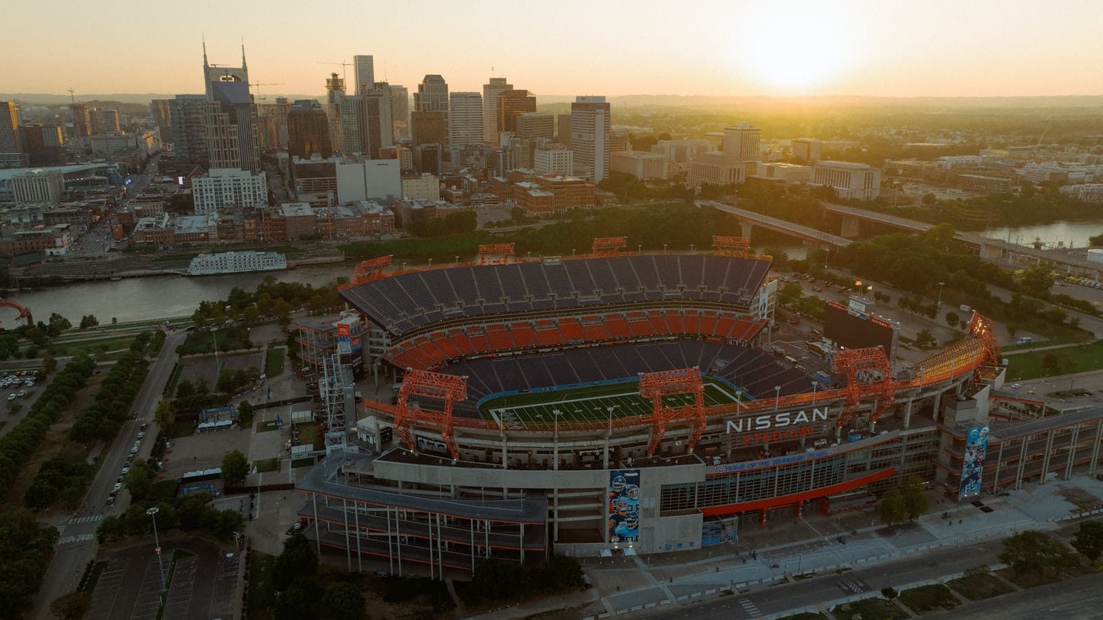 Vista aérea del Nissan Stadium en Nashville al atardecer con el horizonte del centro y el río Cumberland al fondo.