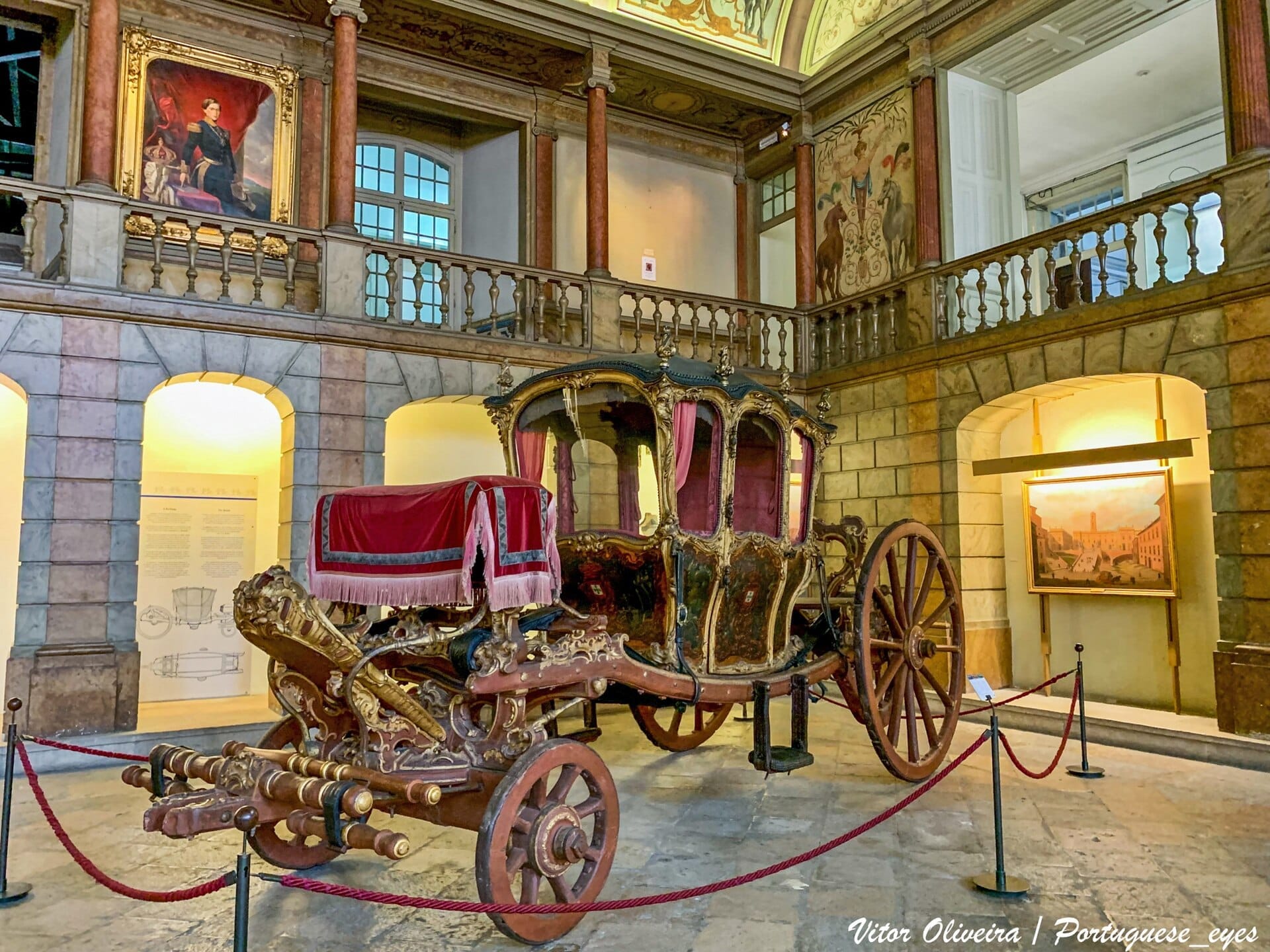 Sontuosa carrozza reale esposta al Museu Nacional dos Coches di Lisbona, circondata da dipinti storici, colonne di marmo e una soffusa illuminazione museale.