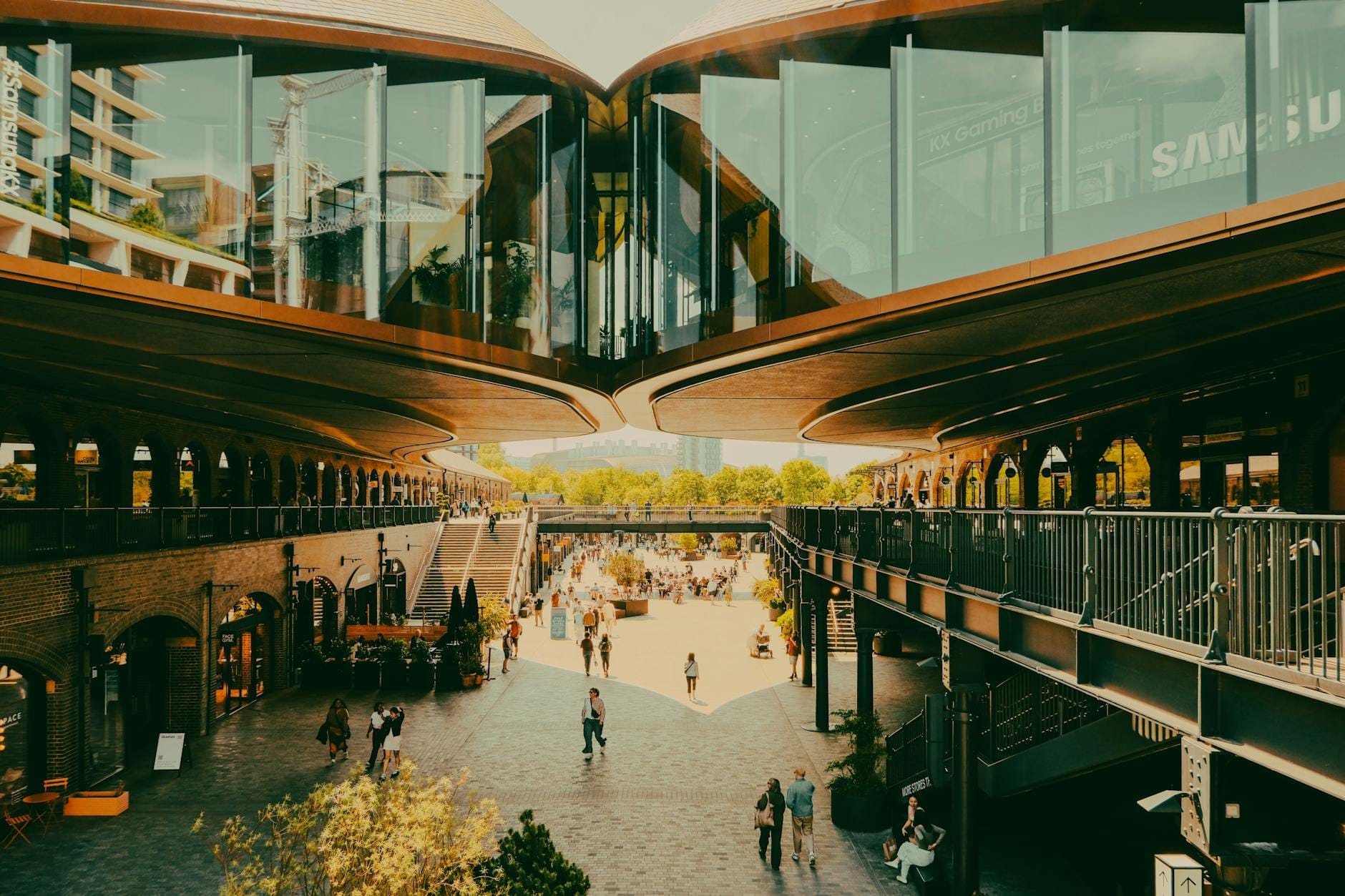 Vista panoramica del cortile centrale di Coal Drops Yard con l'architettura vittoriana restaurata, le passerelle sopraelevate, i negozi e le persone che si godono lo spazio all'aperto.