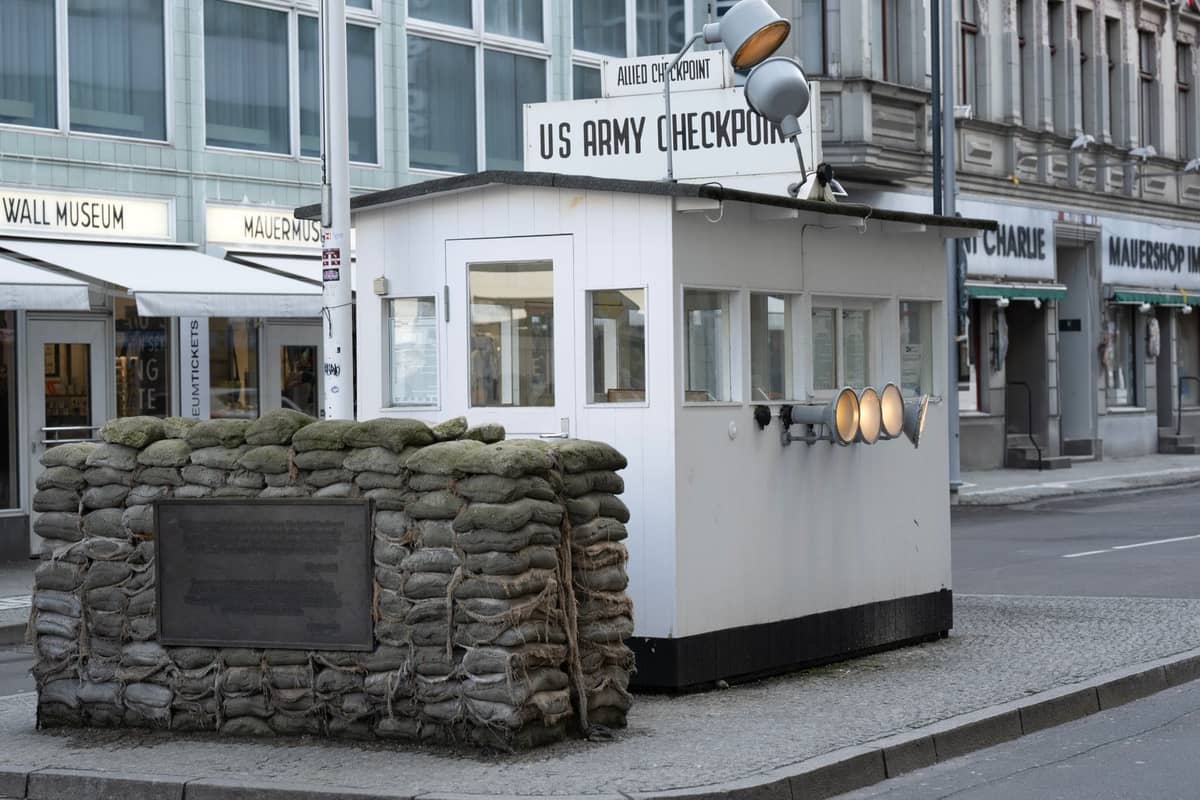 Wachhäuschen am Checkpoint Charlie mit Sandsäcken und der umliegenden Berliner Straße, einschließlich sichtbarer Beschilderung für das Mauermuseum und Geschäfte.
