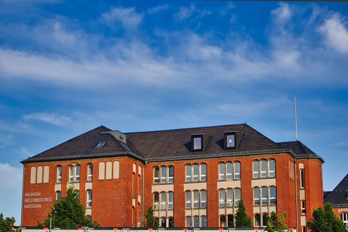 Backsteingebäude unter blauem Himmel mit Schild 'Historisches Museum', belaubte Bäume davor; markanter institutioneller Charakter, typisch für ehemalige Stasi-Standorte.