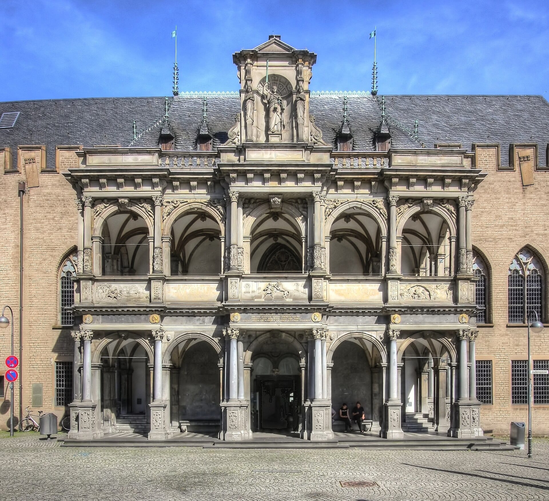 ด้านหน้าของศาลาว่าการเมือง Cologne พร้อมด้วยระเบียง Renaissance โค้งงาม งานหินแกะสลักประณีต และหน้าต่างแบบ Gothic ในวันที่แดดส่องสว่างในย่านเมืองเก่า Cologne