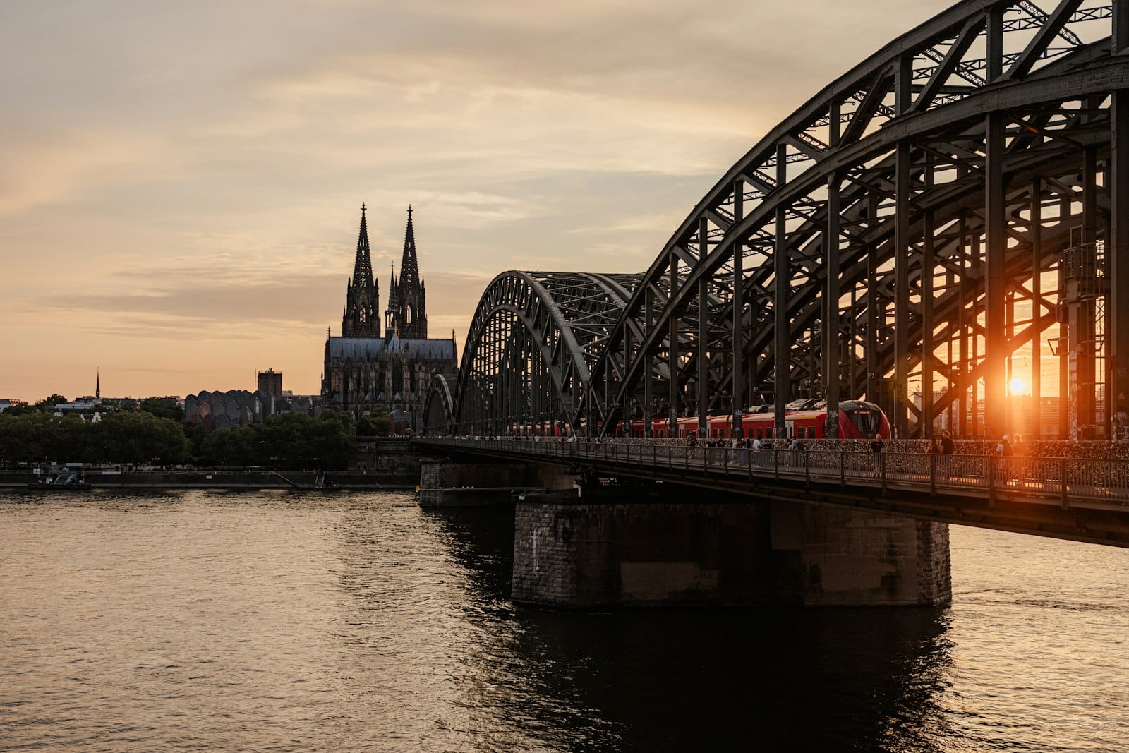 อาสนวิหารโคโลญและสะพาน Hohenzollern เหนือแม่น้ำ Rhine ในยามพระอาทิตย์ตก พร้อมแสงอบอุ่นที่สะท้อนบนผิวน้ำ