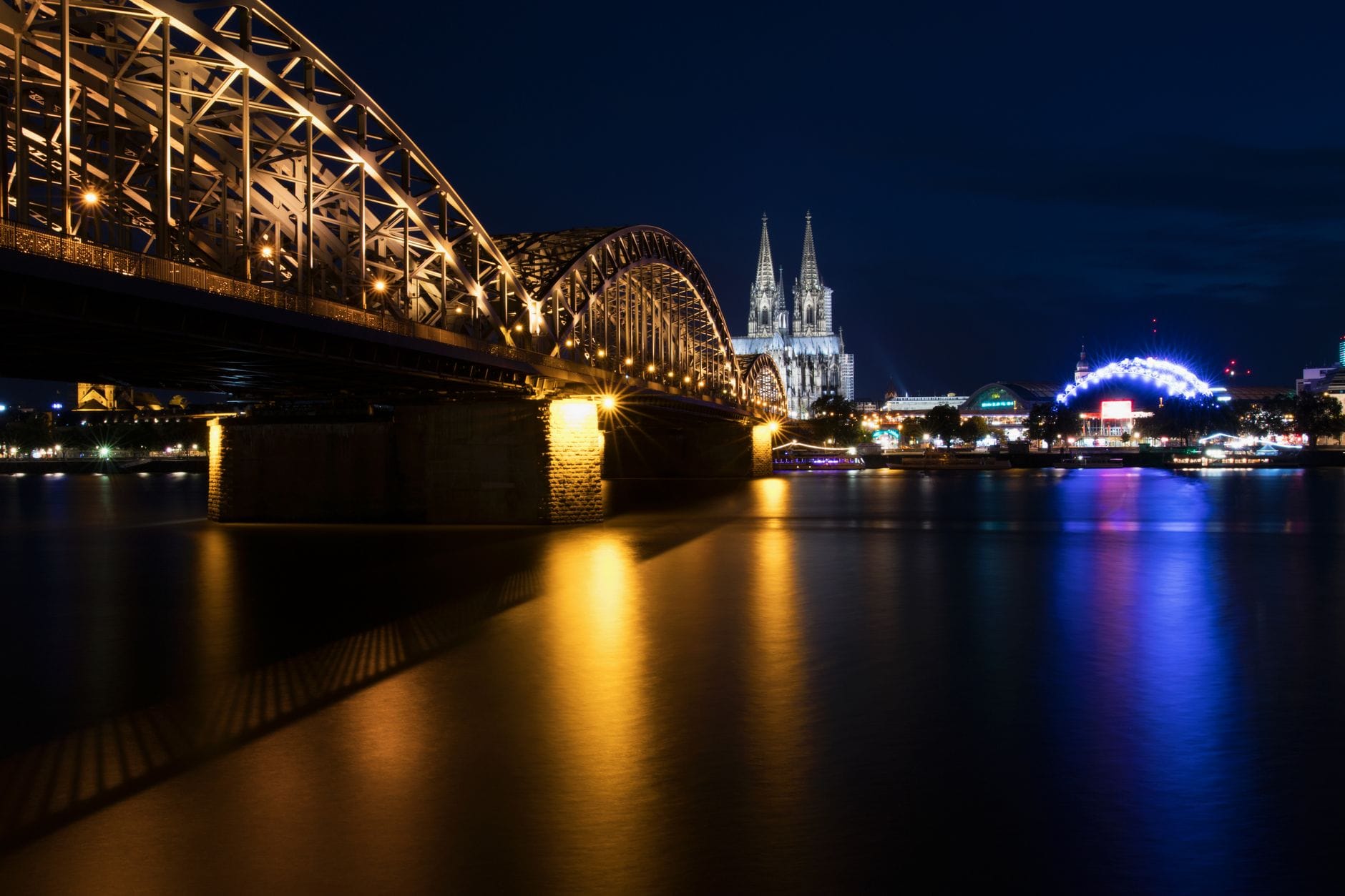 ภาพกลางคืนของมหาวิหารโคโลญจน์และสะพาน Hohenzollern ส่องสว่างสะท้อนแสงบนแม่น้ำไรน์ บรรยากาศปาร์ตี้ยามค่ำของโคโลญจน์