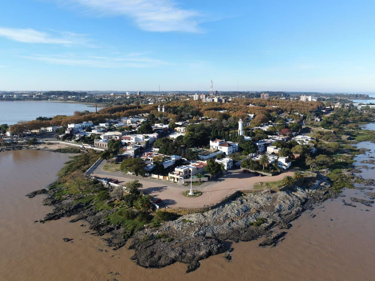 ภาพมุมสูงของ Colonia del Sacramento เห็นคาบสมุทรเมืองเก่าติดน้ำ ประภาคาร ชายฝั่ง และตึกเล็ก ๆ กระจายตัวอย่างสวยงาม