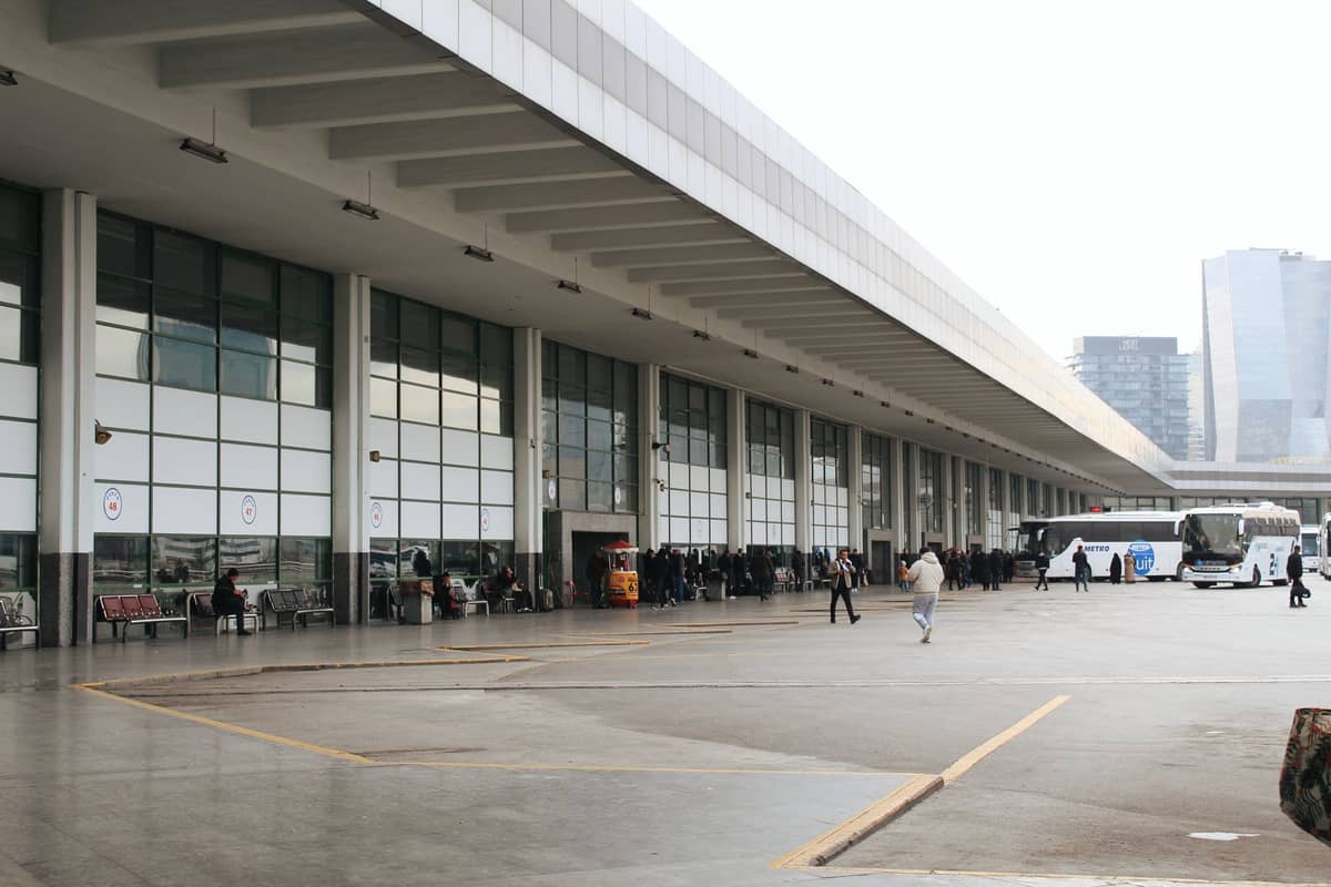 ภายนอกสถานีขนส่งผู้โดยสารที่ยาวและทันสมัย พร้อมผู้คนและรถบัส น่าจะเป็นสถานี Tres Cruces ของมอนเตวิเดโอในวันที่มีเมฆมาก