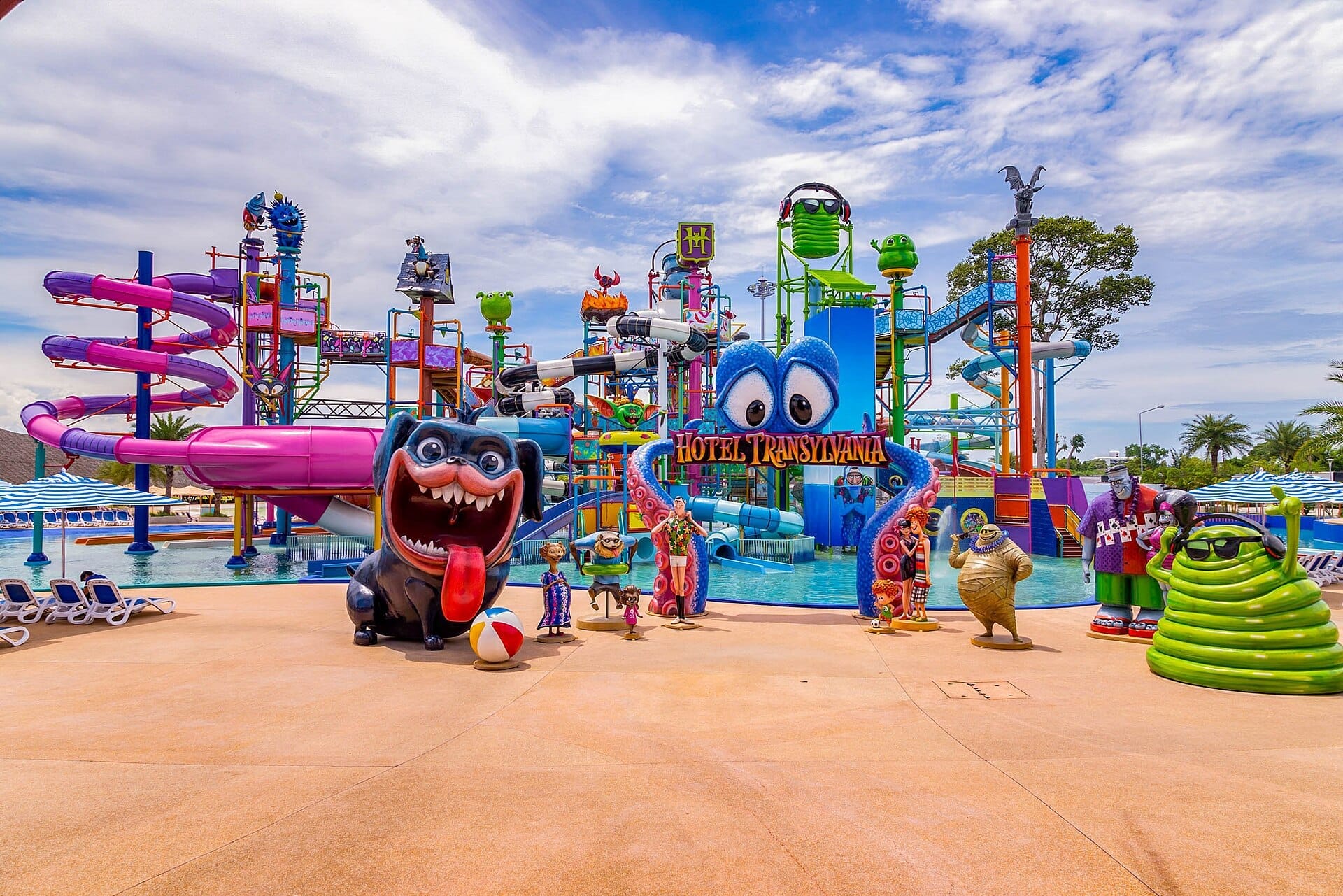 Scivoli d'acqua colorati, personaggi dei cartoni animati giocosi e un cartello di Hotel Transylvania al parco acquatico Columbia Pictures Aquaverse sotto un cielo parzialmente nuvoloso.