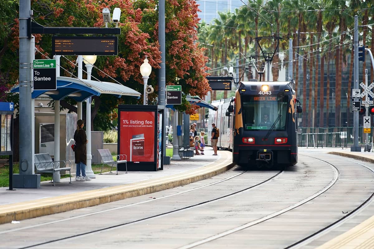 San Diego Straßenbahn an einer Verkehrsstation mit Palmen und wartenden Menschen auf dem Bahnsteig.