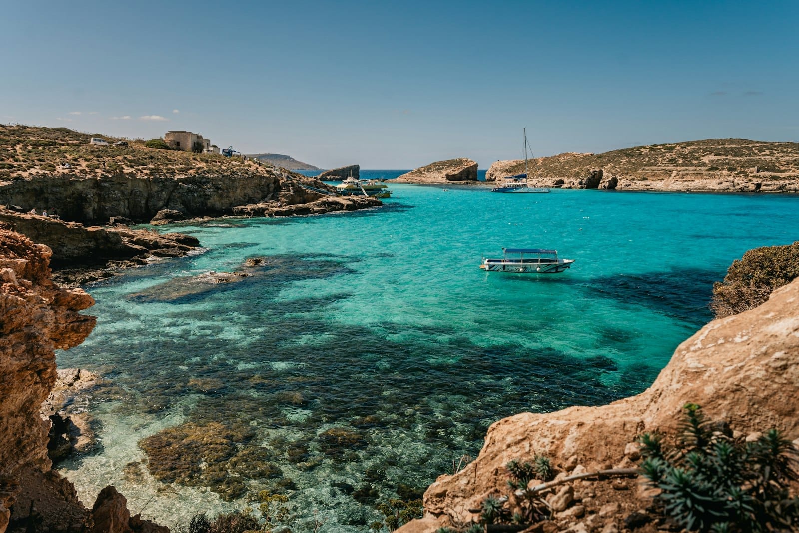 น้ำทะเลสีฟ้าครามใสของ Blue Lagoon ที่โคมิโน มีแนวชายฝั่งหินและท้องฟ้าใสสด พร้อมแพลอยน้ำในลากูน