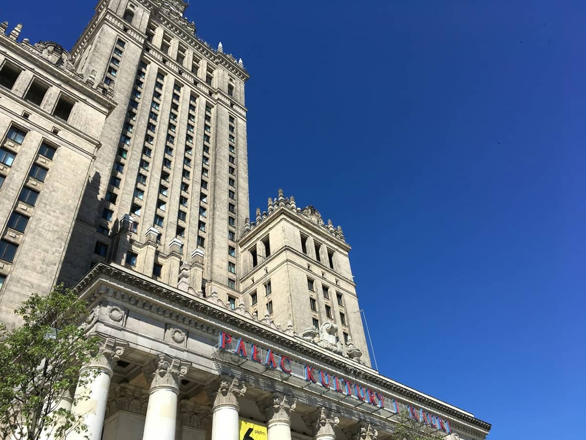 Hohes Steingebäude mit Türmen und Säulen unter einem klaren blauen Himmel, das den Palast der Kultur und Wissenschaft im Zentrum von Warschau zeigt.