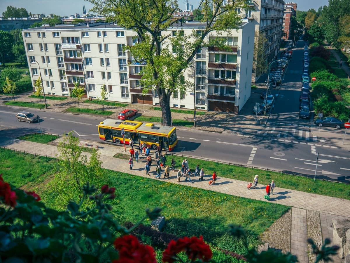 Blick auf eine breite Allee mit Wohnblöcken aus der Mitte des Jahrhunderts und Menschen, die in der Nähe eines gelben Stadtbusses spazieren, typisch für sozialistische Wohngebiete der Nachkriegszeit.