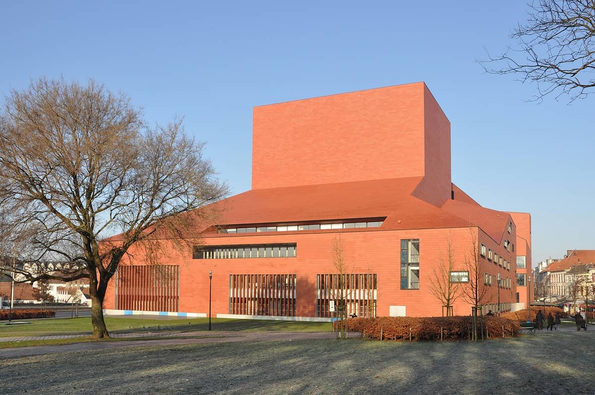 The modern red-brick Concertgebouw Brugge stands prominently on 't Zand square, framed by bare winter trees and a clear blue sky.