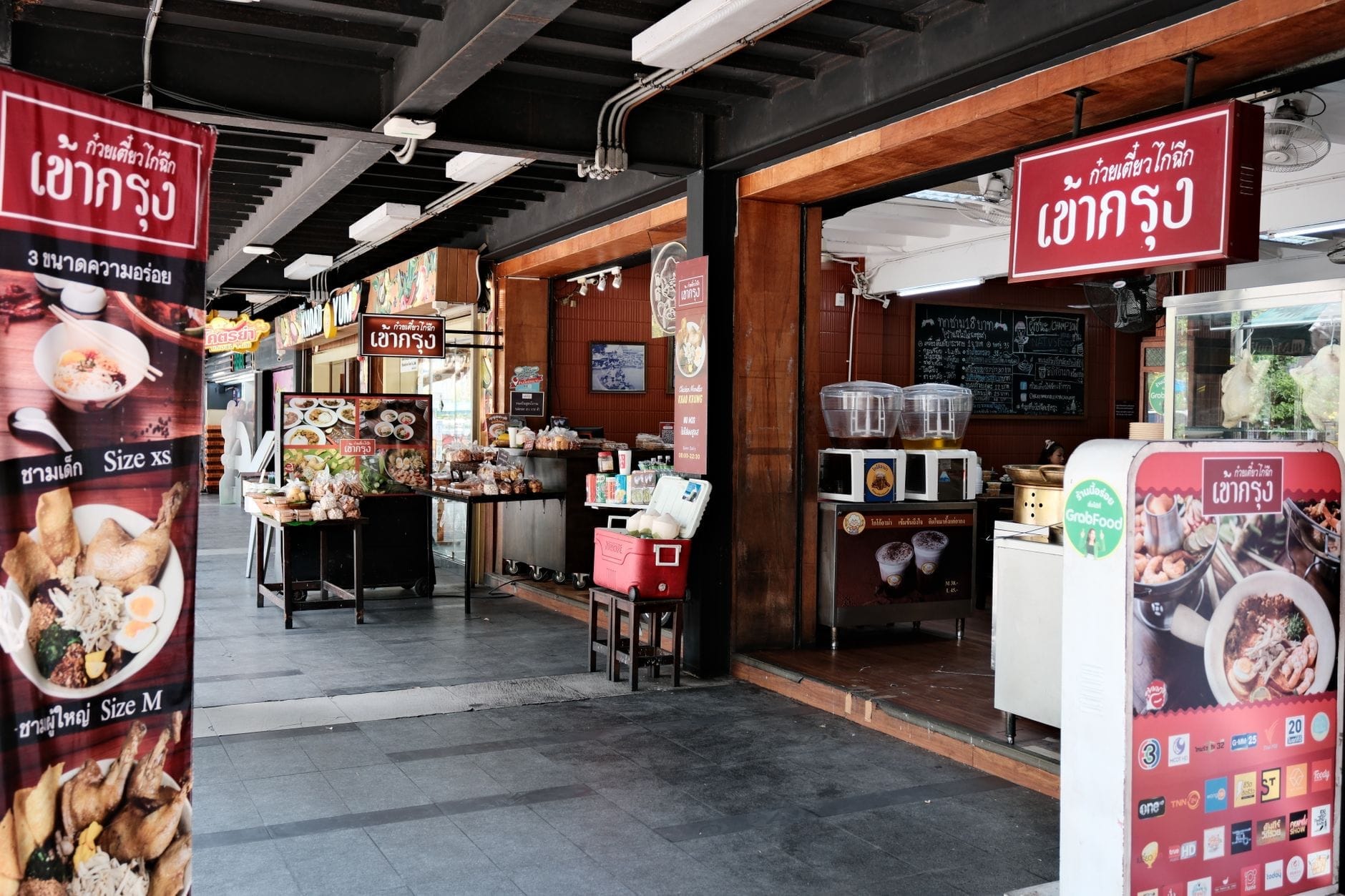 Restaurante tailandés luminoso y abierto al frente con letreros coloridos y exhibición de comida, típico de la animada escena gastronómica de Chiang Mai.